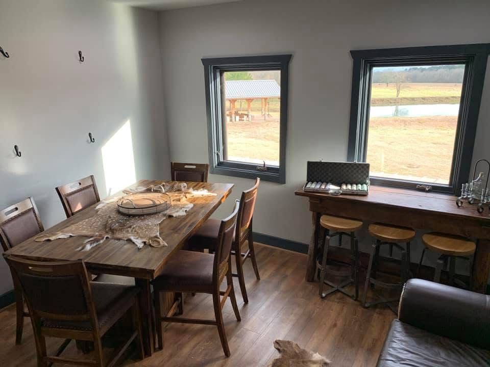 Dining room with two tables, wooden chairs, and large windows looking out onto a yard.