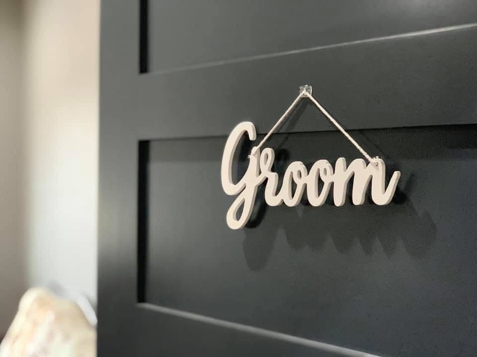 Wooden “Groom” sign hanging on a dark paneled door