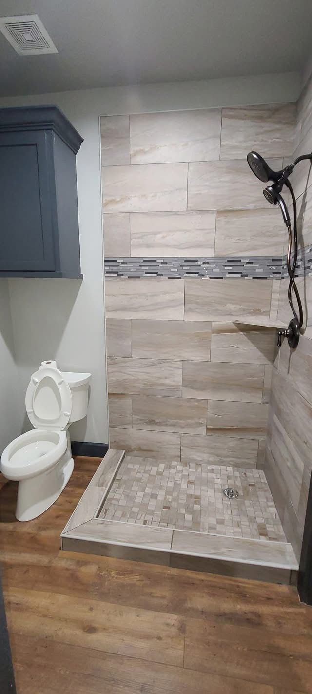 Bathroom with toilet beside a tiled walk-in shower and wood-look floor