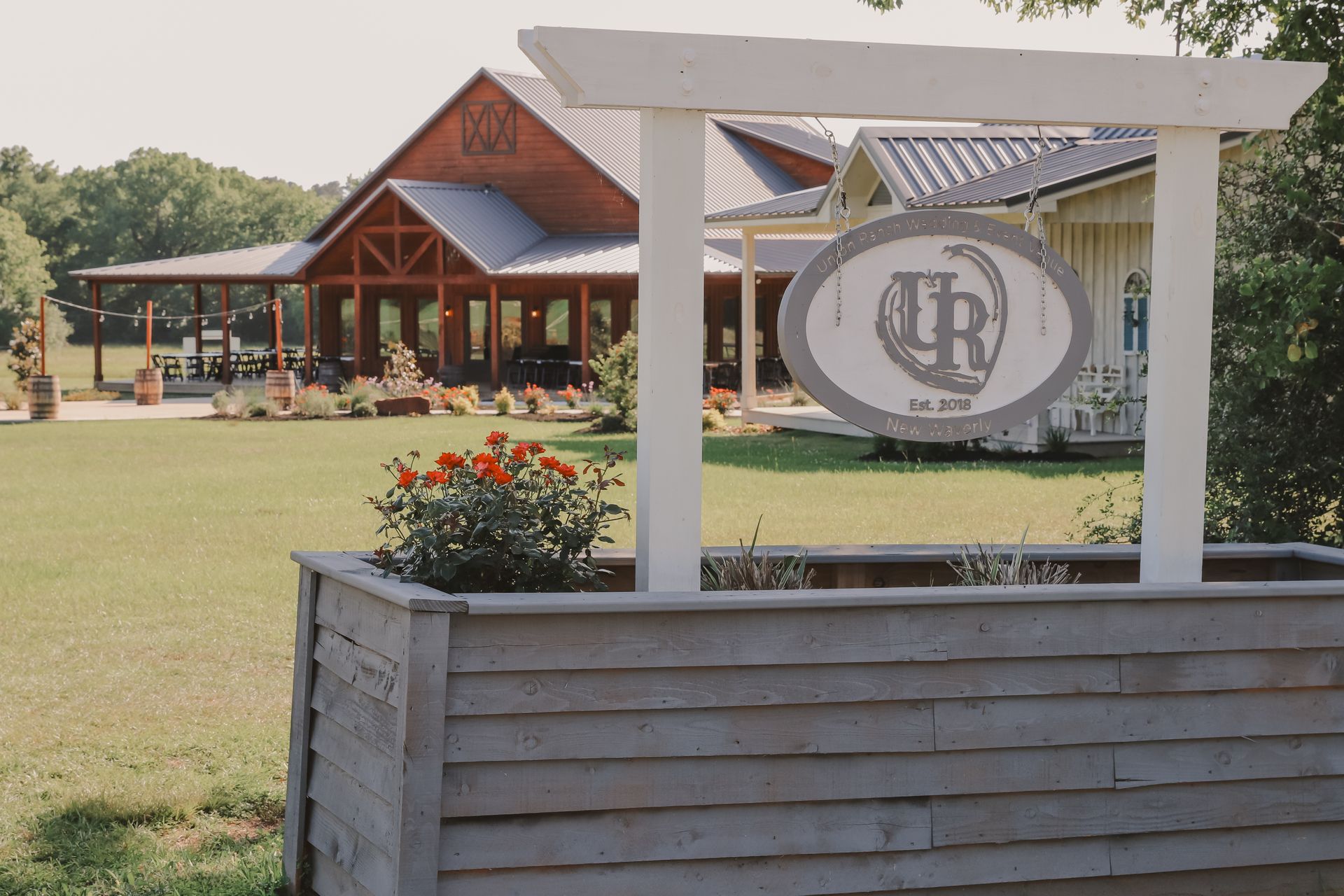 Rustic lodge entrance with wooden sign, flower bed, and large logo banner on a lawn