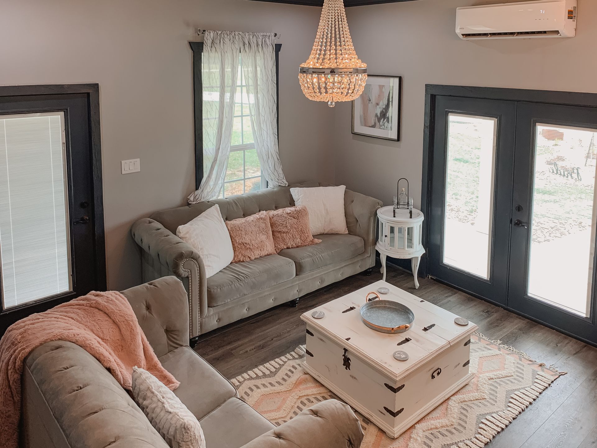 Cozy living room with gray sofa, armchair, white coffee table, patterned rug, and large windows with curtains