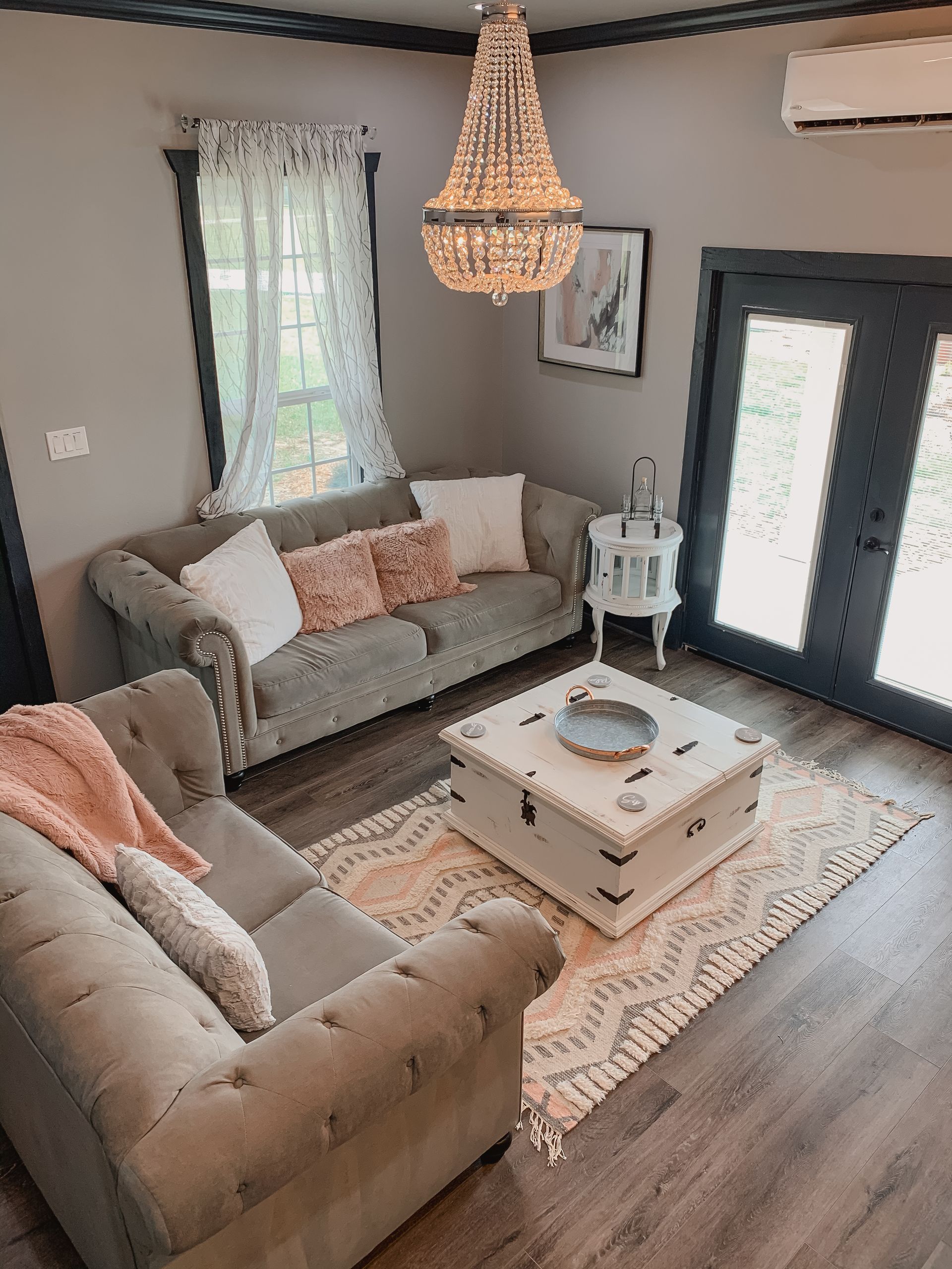 Cozy living room with beige sofas, wicker chandelier, white coffee table, patterned rug, and French doors.