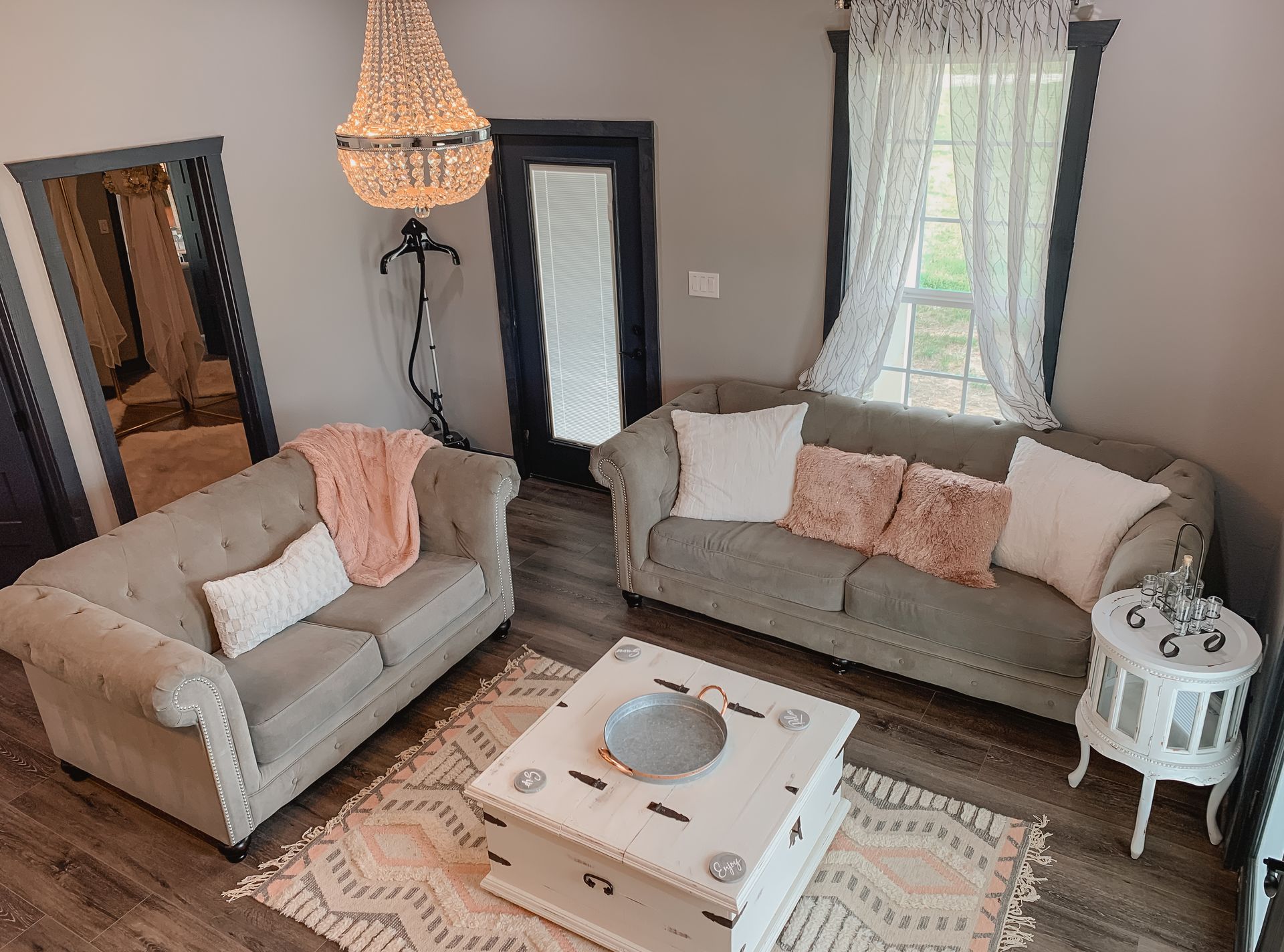 Cozy living room with beige sofas, pink pillows, chandelier, mirror, and patterned rug