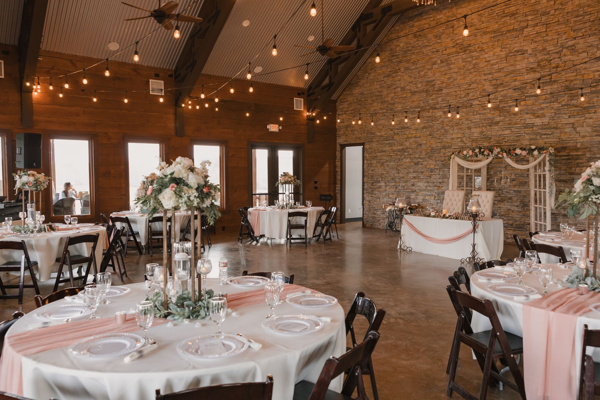 Elegant rustic wedding reception hall with round tables, white linens, and floral centerpieces
