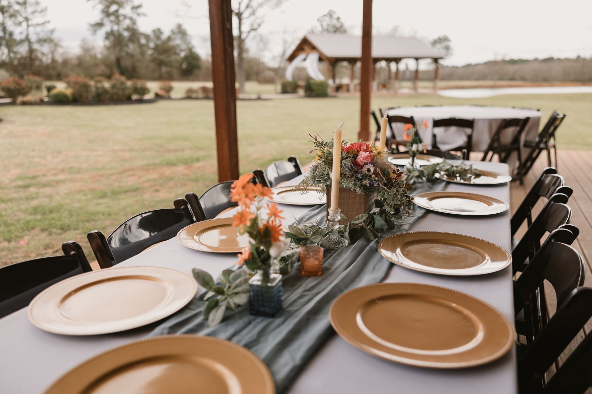 Long outdoor dining table set with plates, candles, and autumn floral centerpieces under a patio
