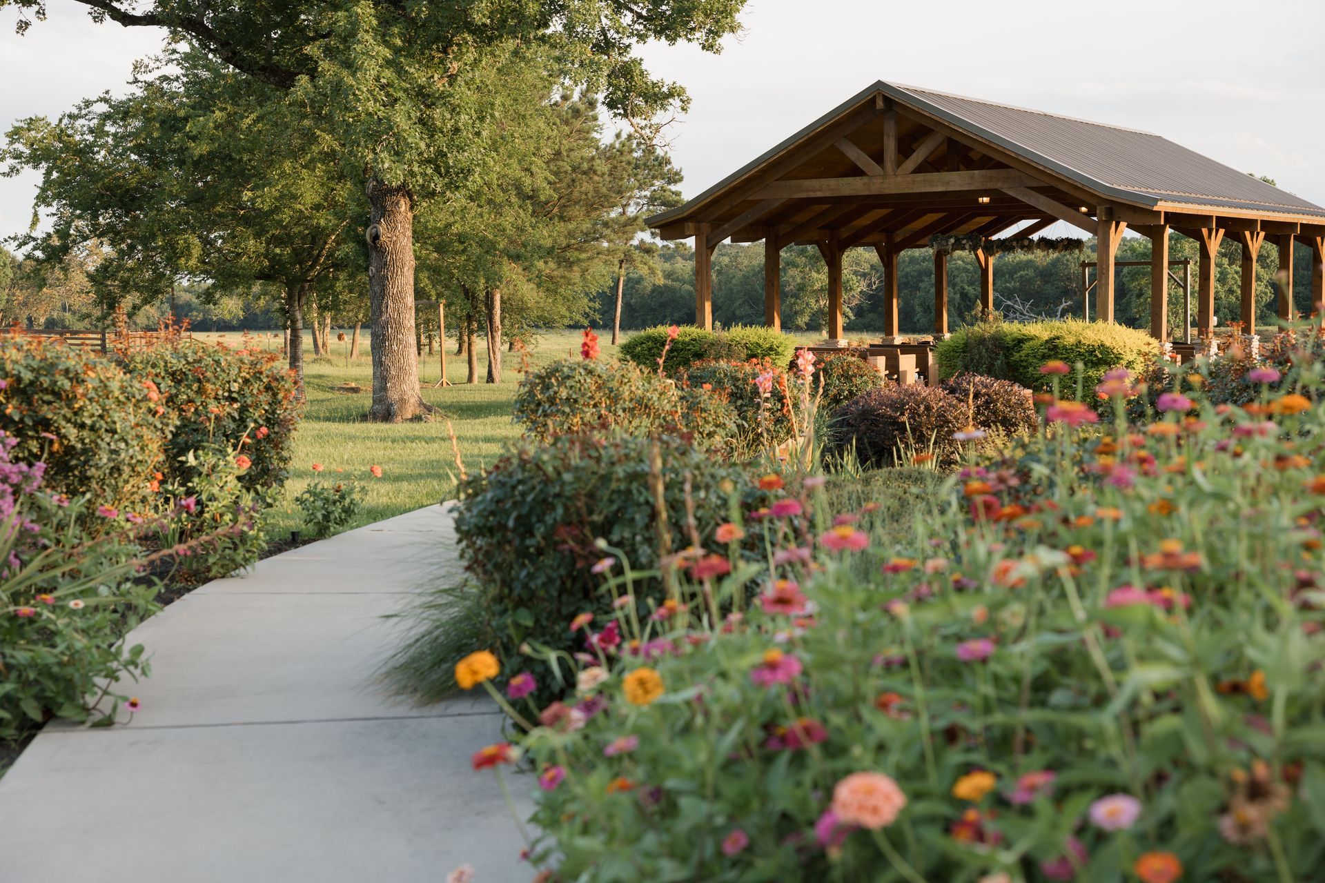 Garden path beside wildflowers leading to a wooden pavilion in a sunny park