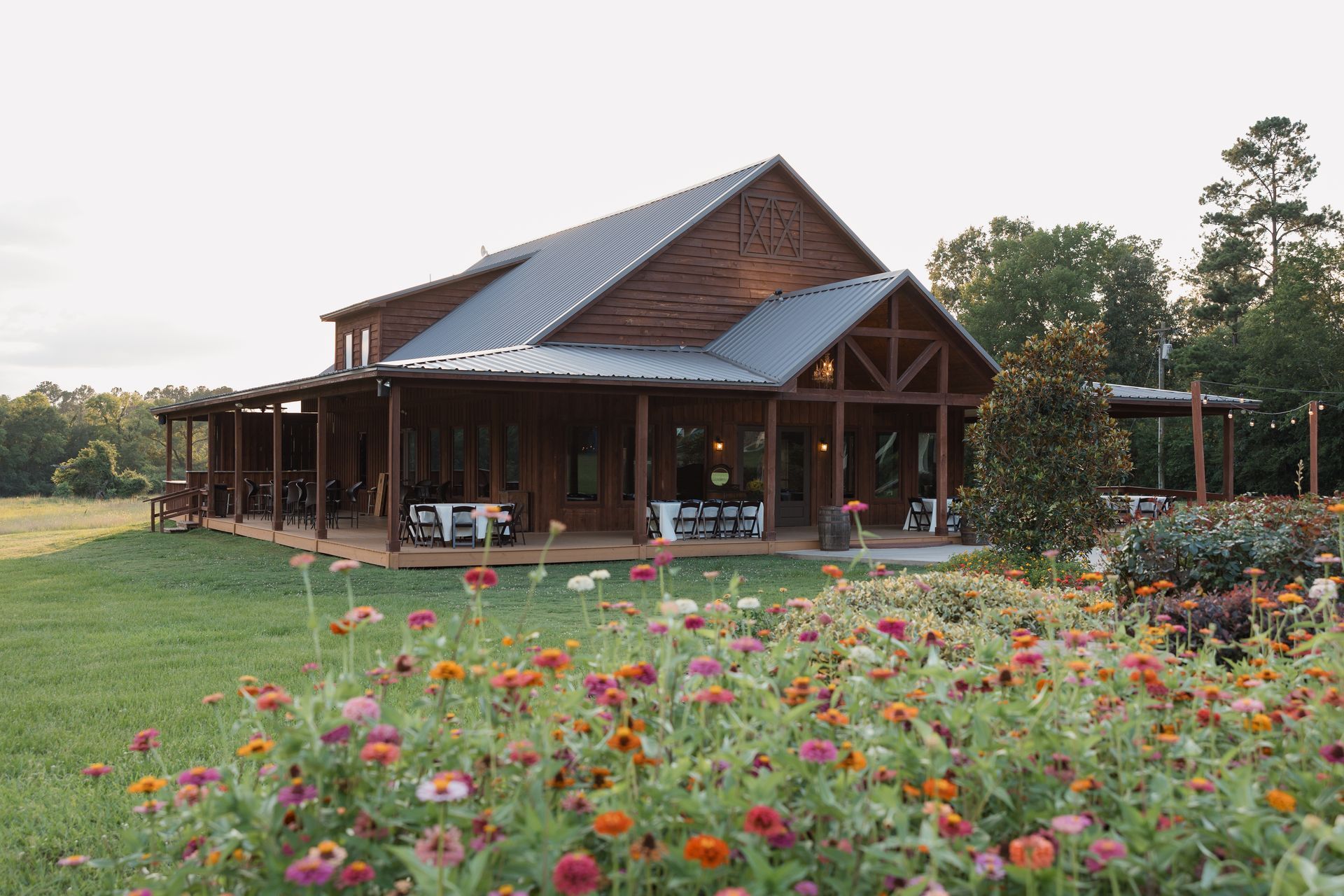 Wooden house with a blue roof beside a flower garden and grassy yard at dusk