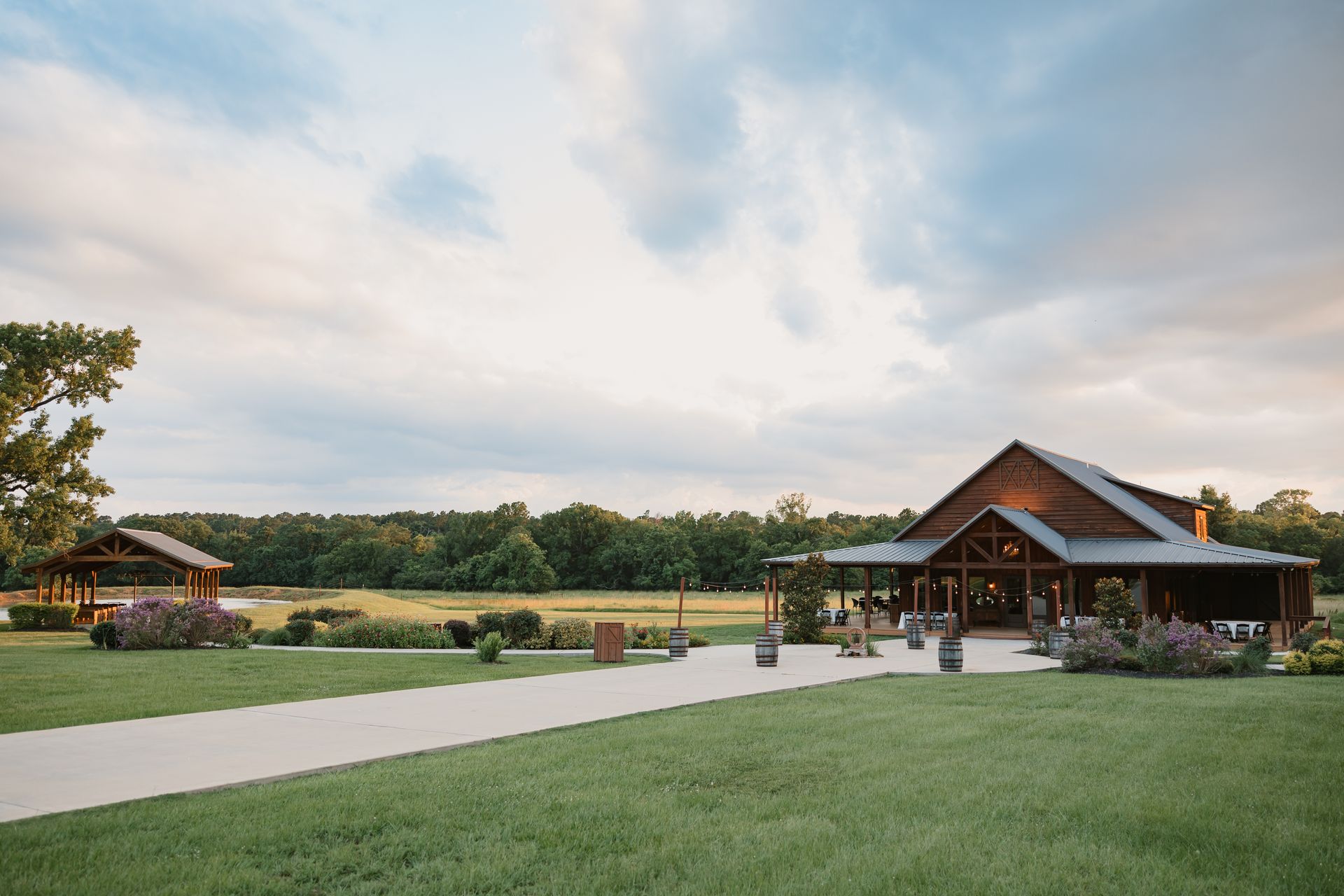 Wide lawn with a wooden pavilion, paved path, and trees under a cloudy sky.