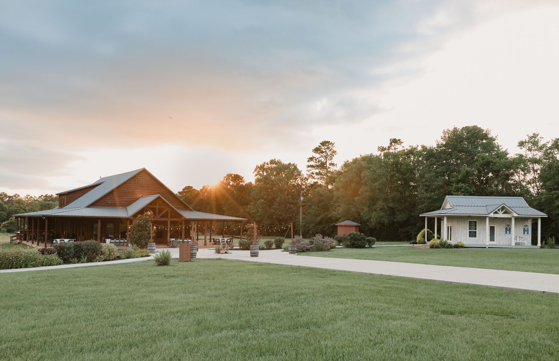 Rustic cabins on a grassy lawn at sunset, with trees and a pale sky.