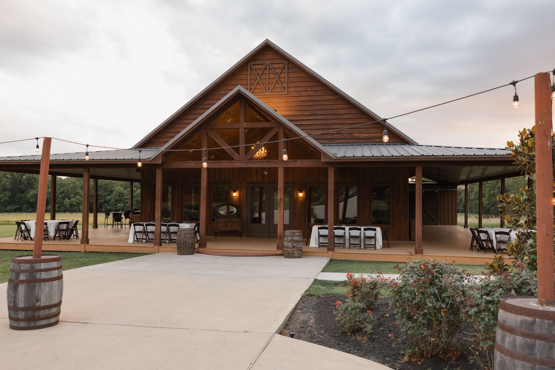 Rustic wooden lodge entrance with benches, string lights, and barrel planters at dusk.