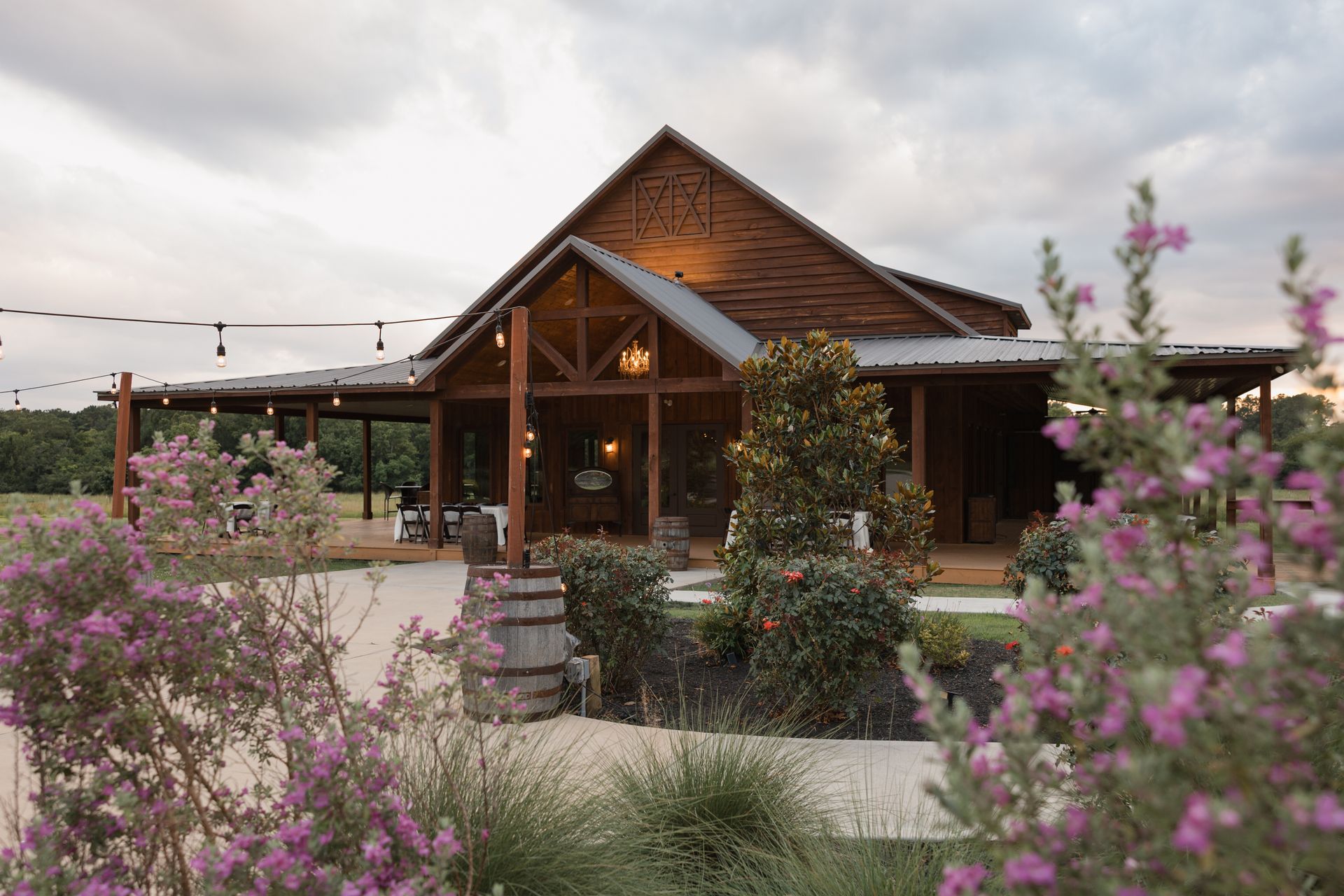 Rustic wooden cabin with a peaked roof, framed by pink flowers and greenery at dusk