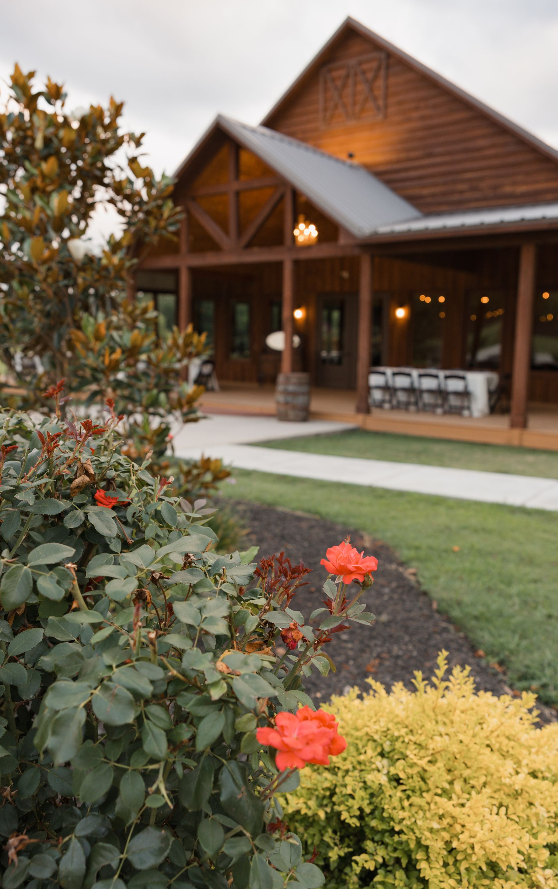 Wooden lodge porch with warm lights, surrounded by flowering shrubs and a green lawn at dusk