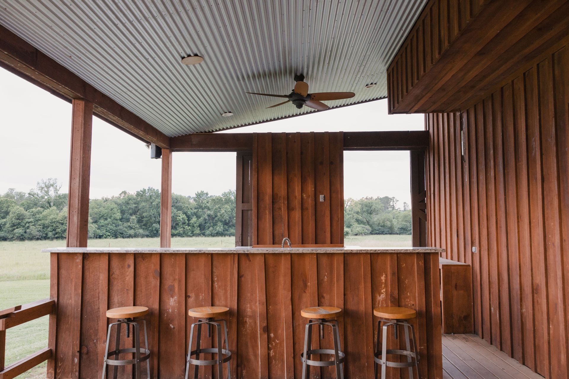 Wooden porch bar with stools overlooking a grassy field and trees