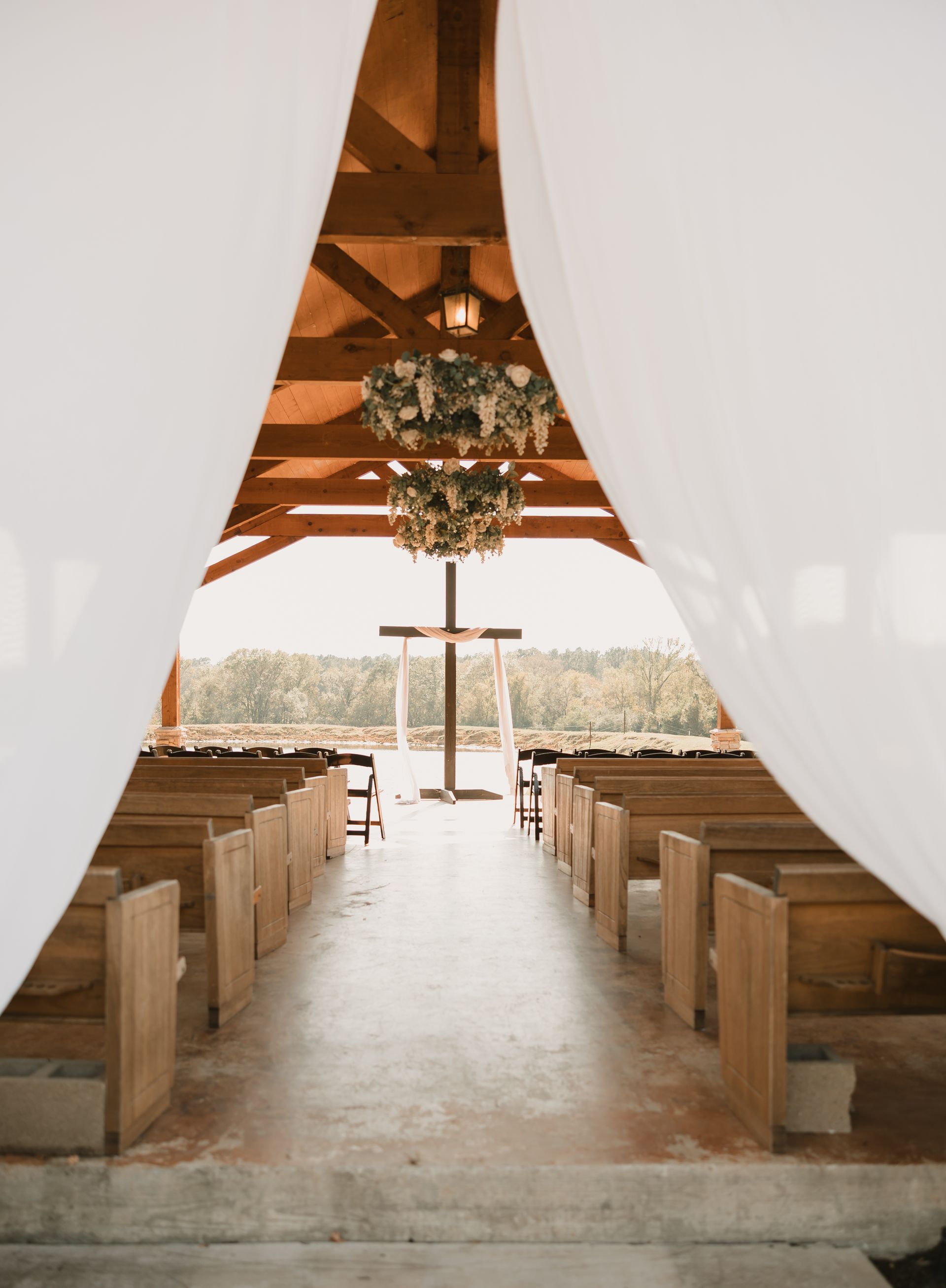 Open-air wooden wedding chapel with white drapes, pews, and floral chandeliers facing a scenic view