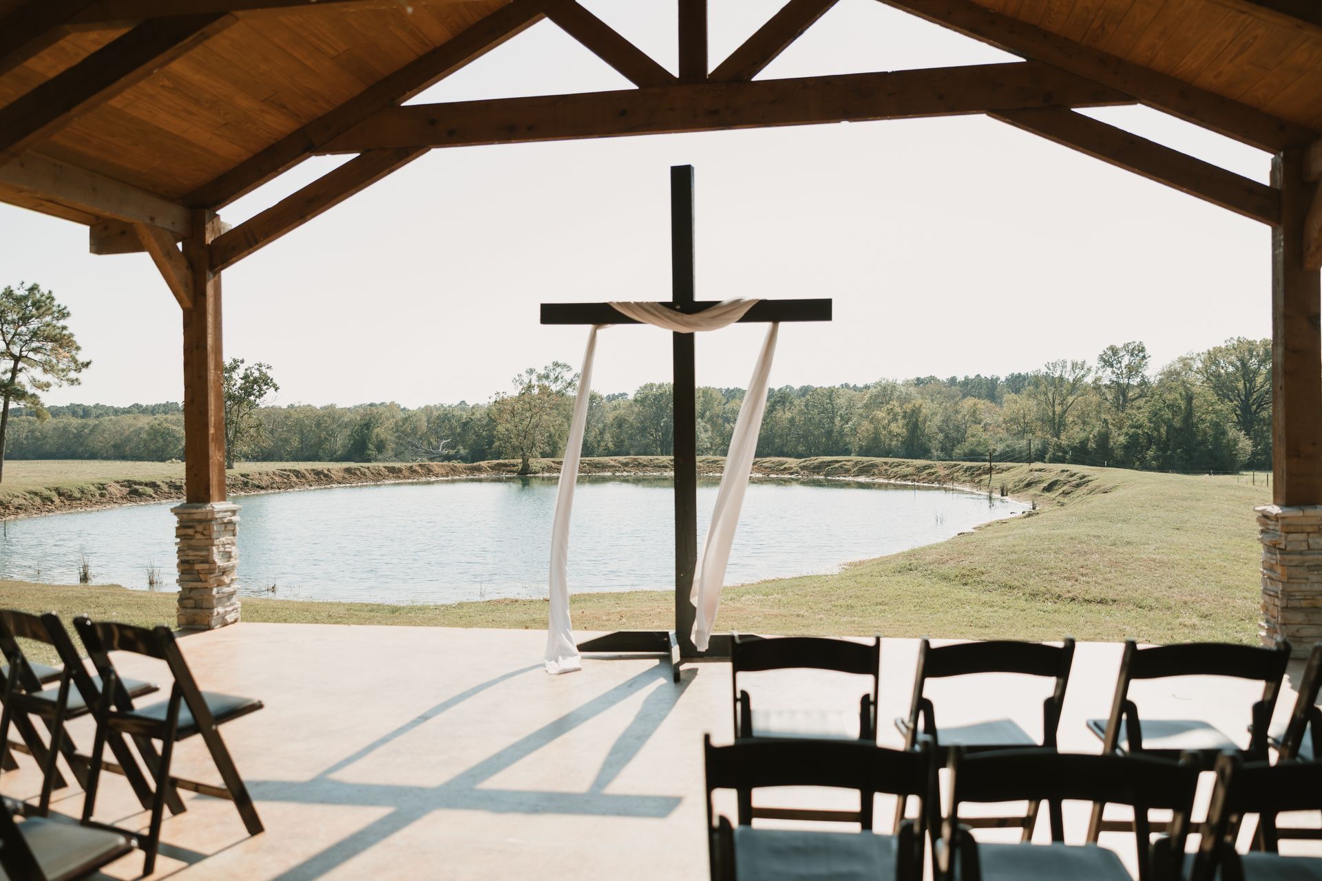 Open-air wedding pavilion overlooking a lake, with chairs and an altar under a wooden roof.