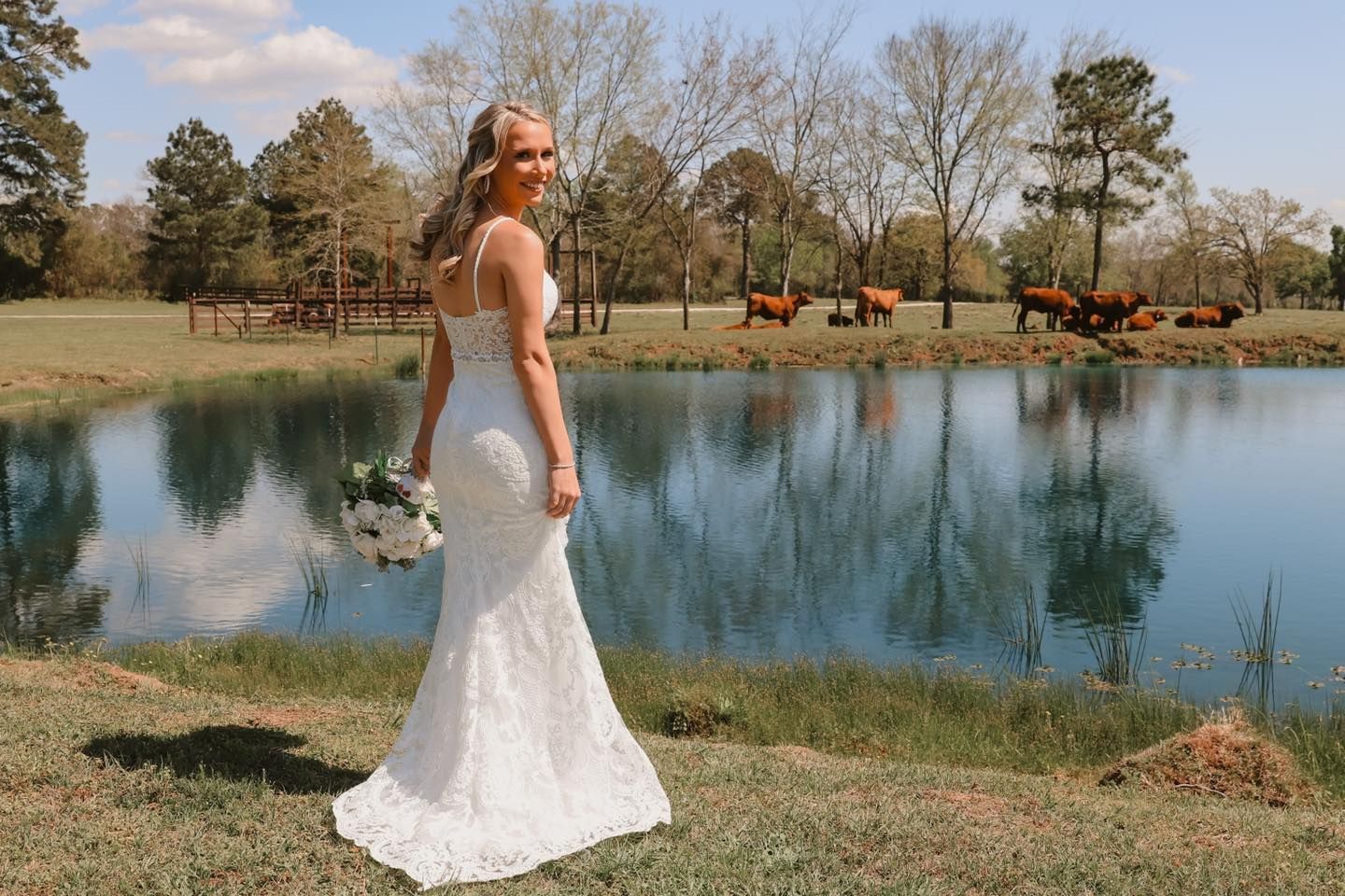 Woman in a white dress standing by a pond with cows and trees in the background