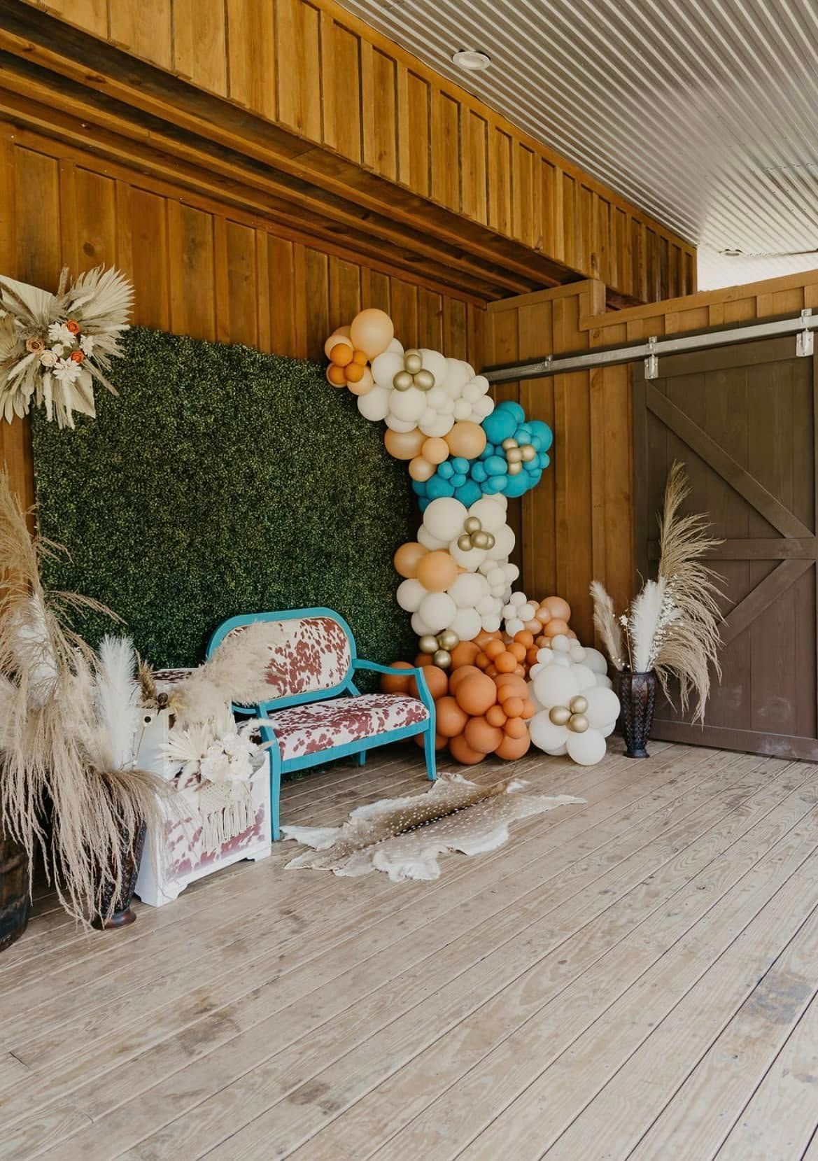 Boho photo backdrop with balloon arch, floral decor, and a turquoise bench in a rustic barn-like space