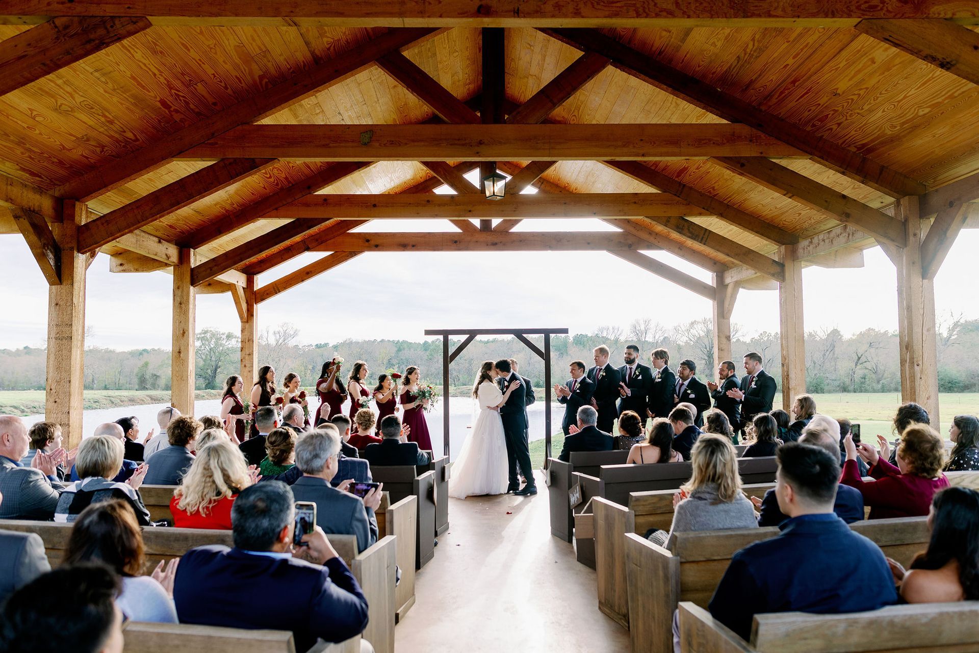 Wedding ceremony in a rustic pavilion, with guests seated and a couple standing at the altar.