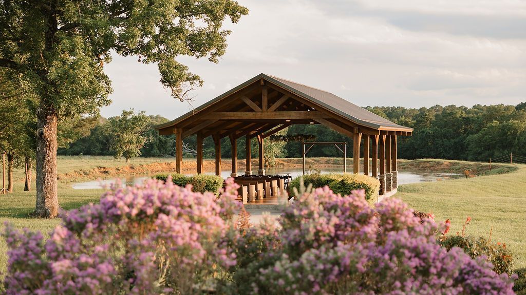 Wooden pavilion in a meadow with pink wildflowers and trees under a soft evening sky