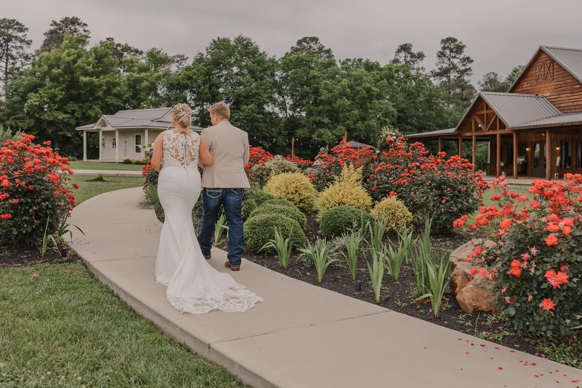 Couple walking on a curved garden path beside red flowers and a rustic wooden pavilion
