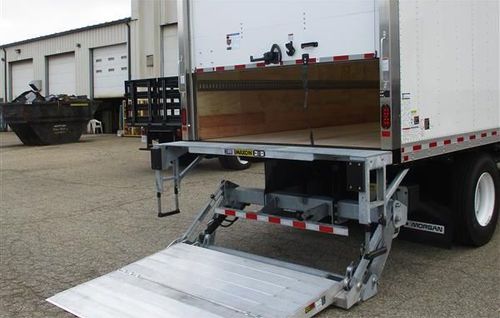 White delivery box truck with open rear lift gate ramp in an industrial lot