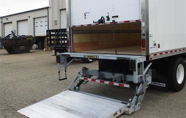 White delivery box truck with open rear lift gate ramp in an industrial lot