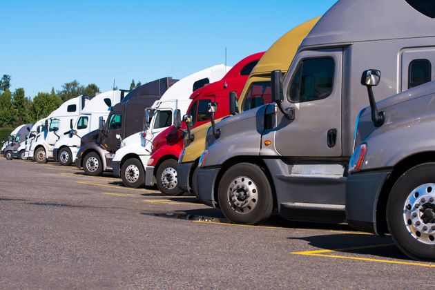 Row of parked semi trucks in white, red, yellow, and gray along a road under a blue sky