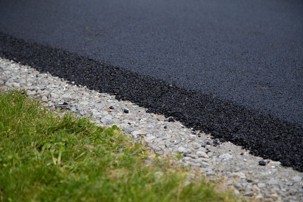 A close up of a black asphalt road with gravel and grass.