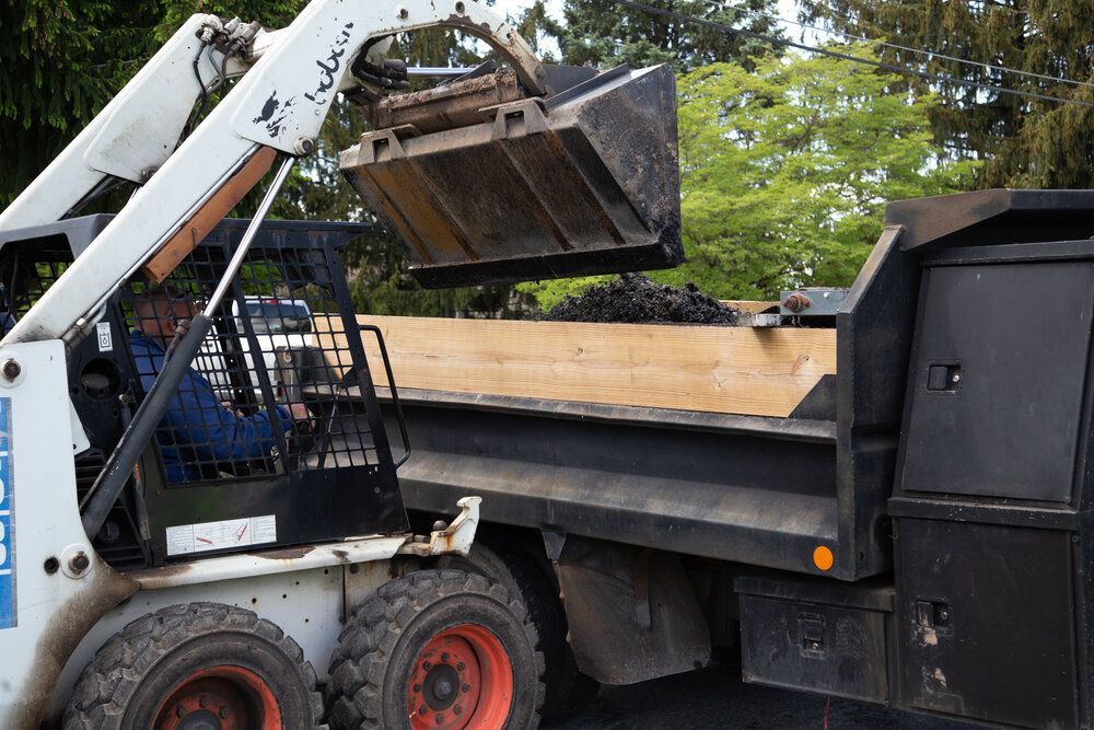 A bobcat is loading dirt into a dump truck.