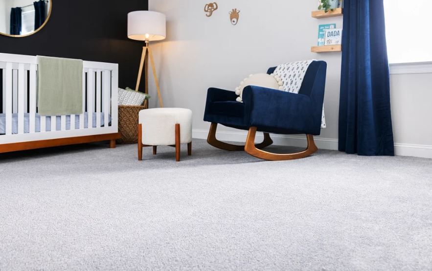 A nursery with a crib, rocking chair, ottoman, and lamp.