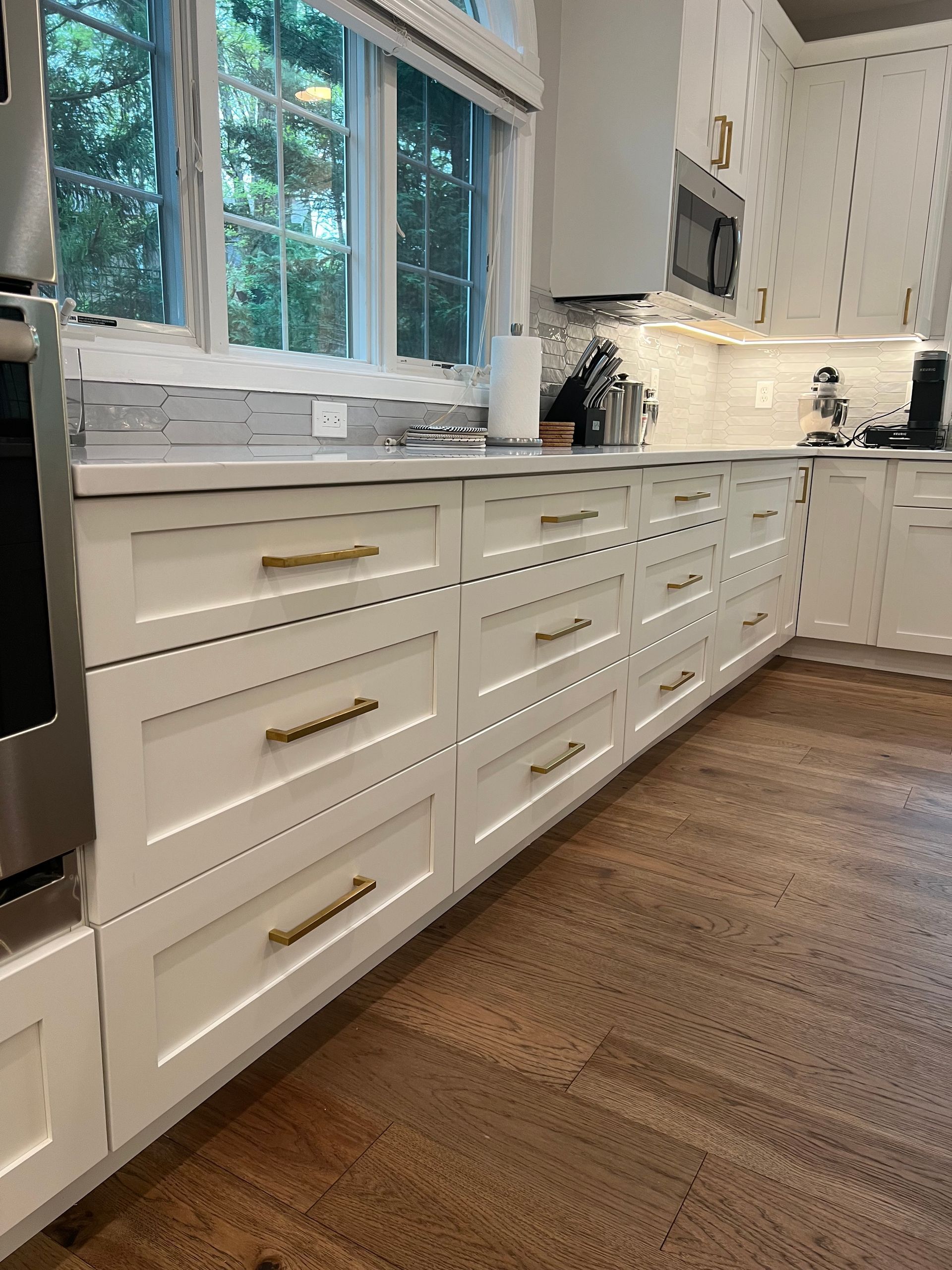 A kitchen with white cabinets, wooden floors, and stainless steel appliances.