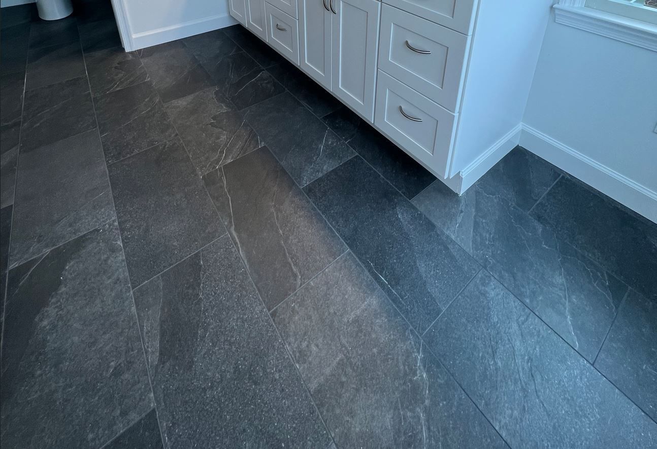 A bathroom with a black tile floor and white cabinets.