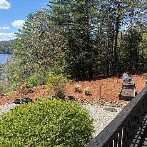 Patio with black railing overlooking a wooded hillside and lake on a sunny day