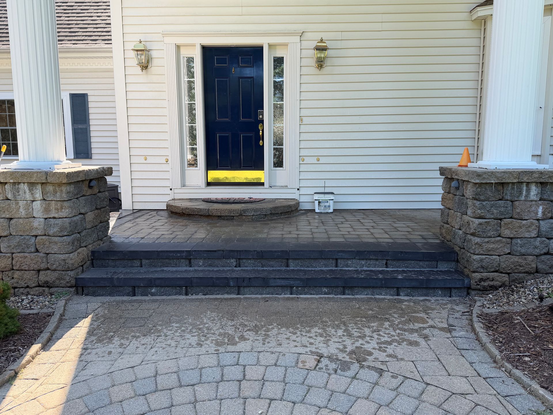 Front entry with blue door, stone steps, and curved paver walkway between stone pillars