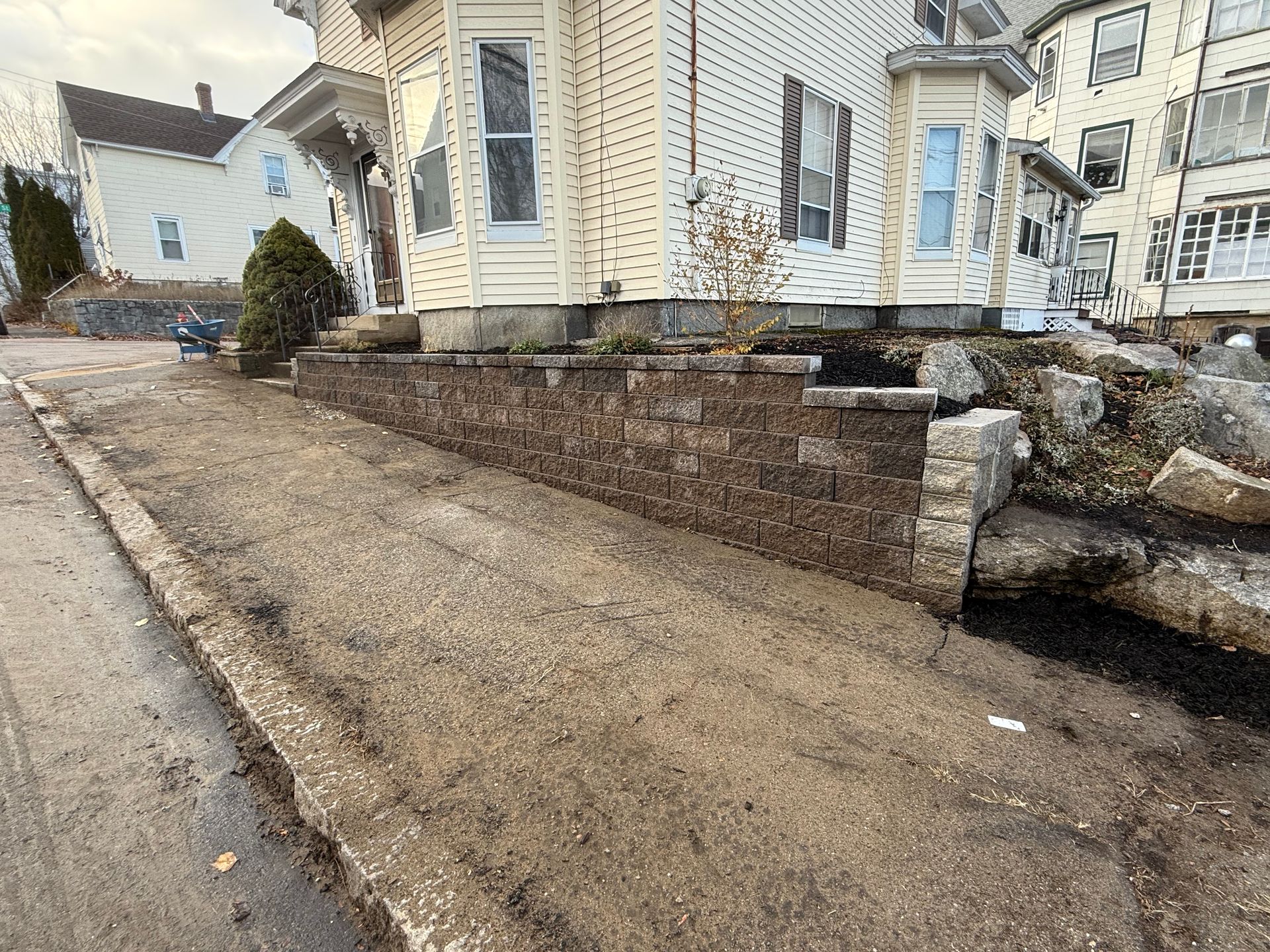 Driveway beside a house with a brick retaining wall and large boulders
