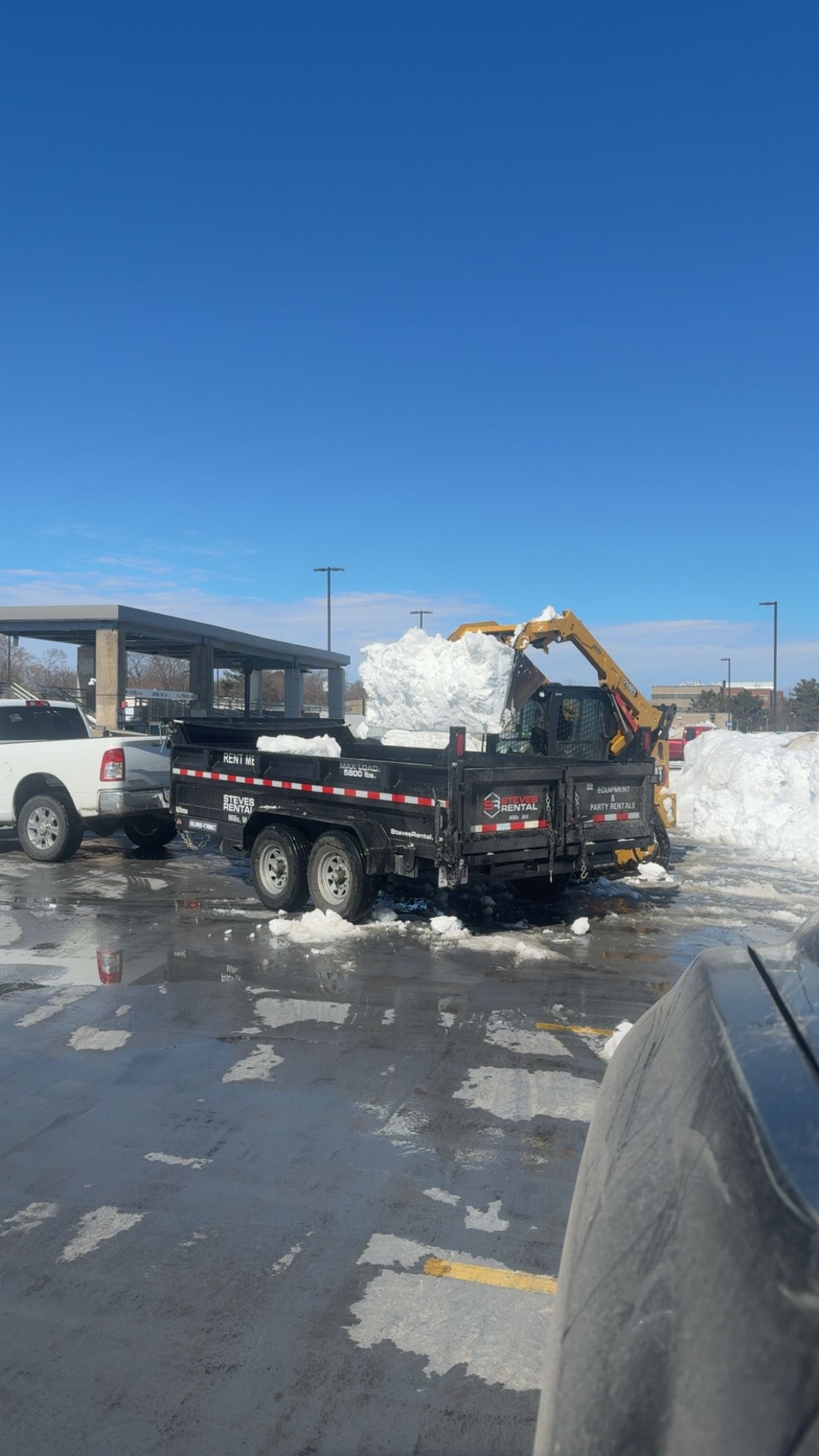 Tow truck loading a white pickup in a snowy parking lot under a clear blue sky