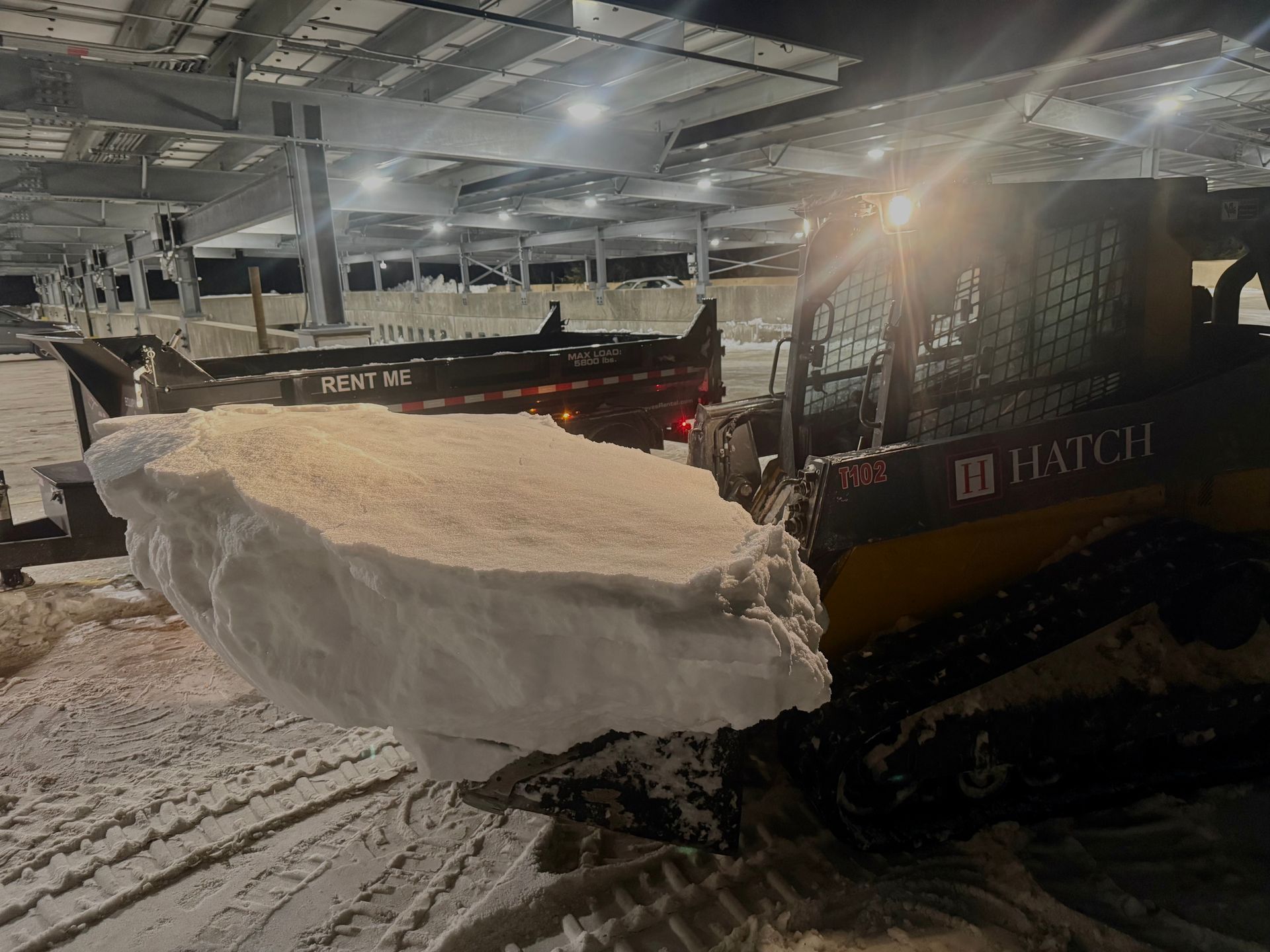Snowplow clearing a large snow pile in a covered parking lot at night