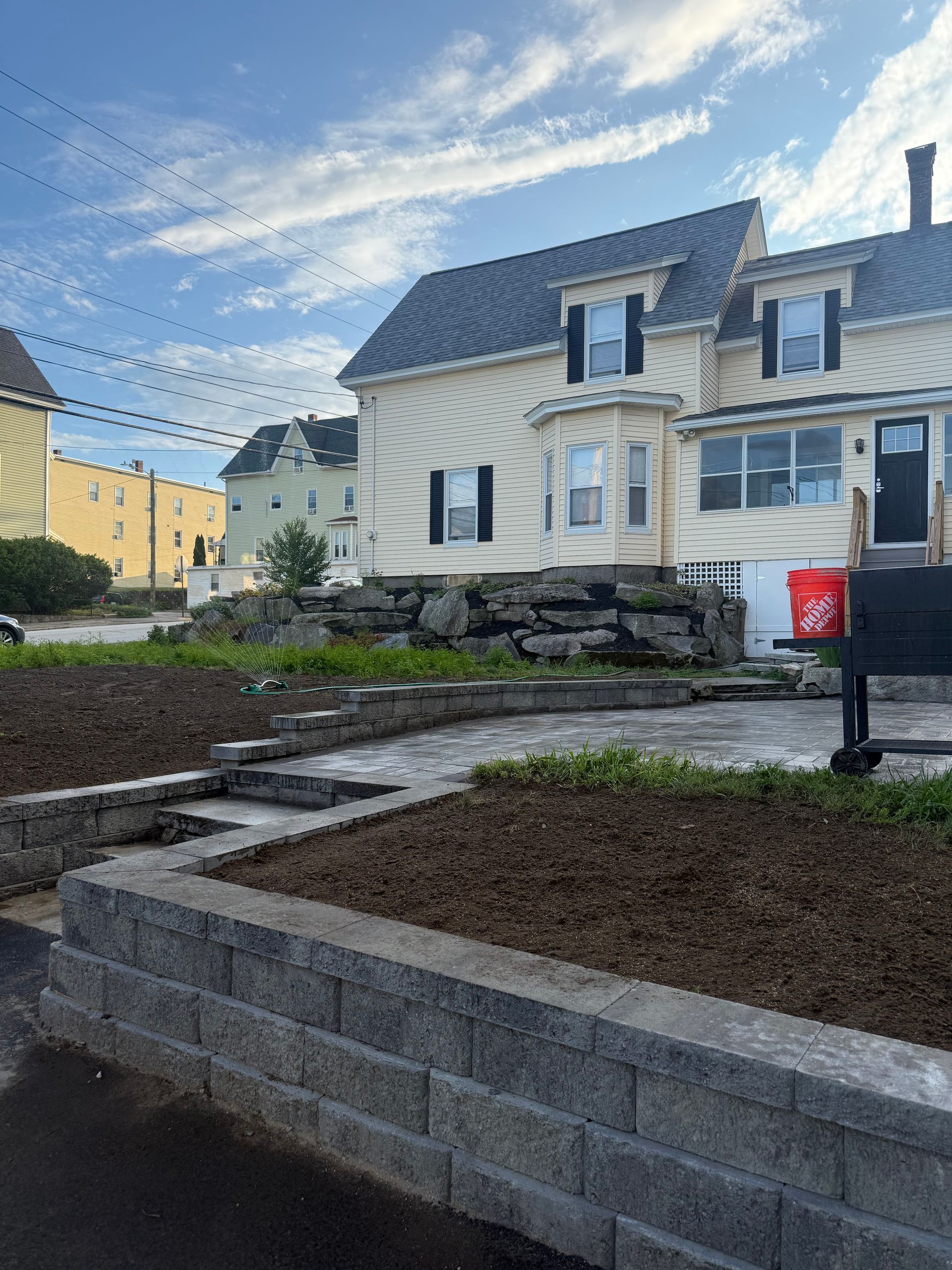 Stone steps and retaining wall leading to a cream house with a blue roof under a bright sky.