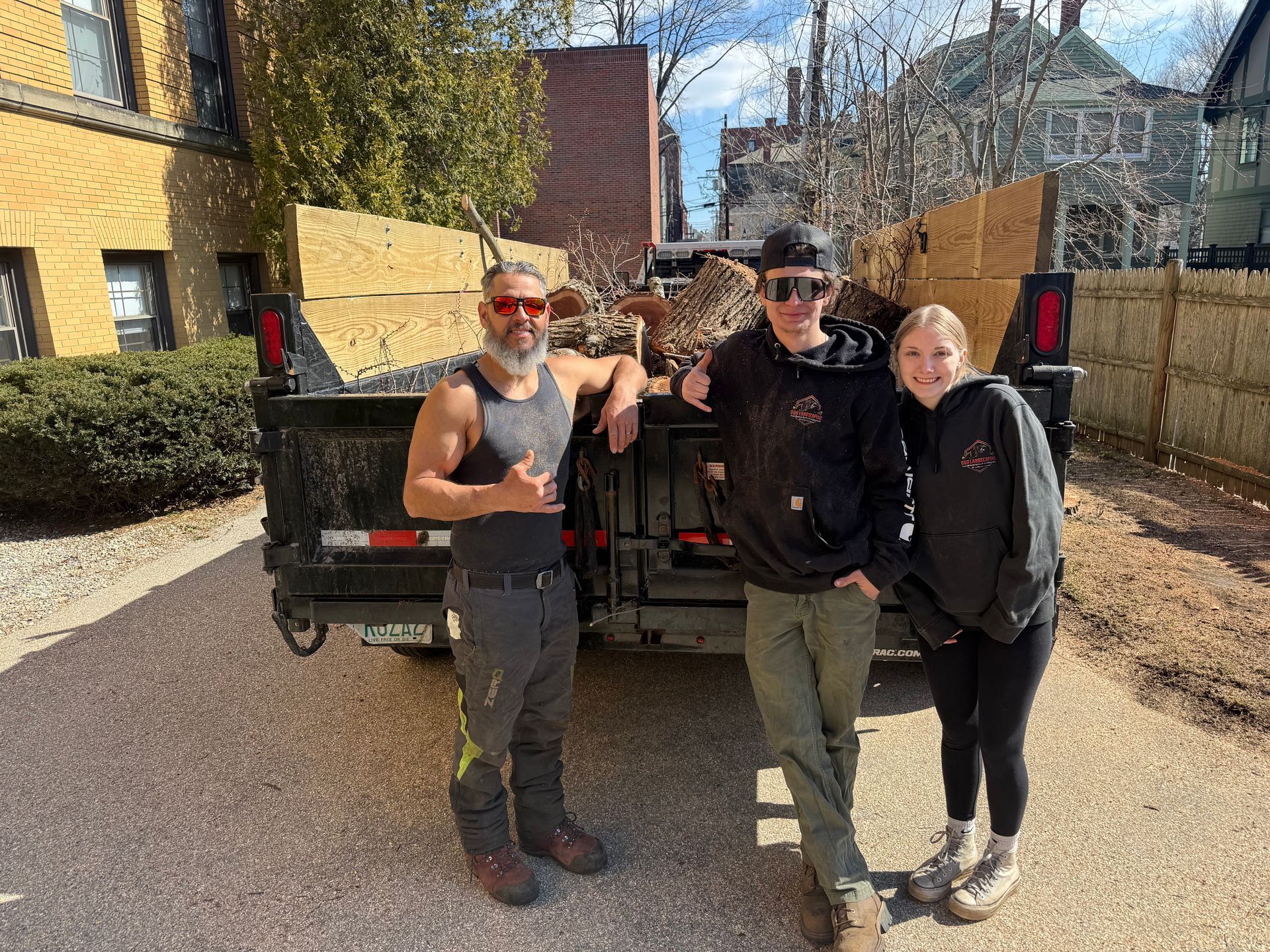 Three people stand smiling in front of a black pickup truck loaded with brush and yard waste.