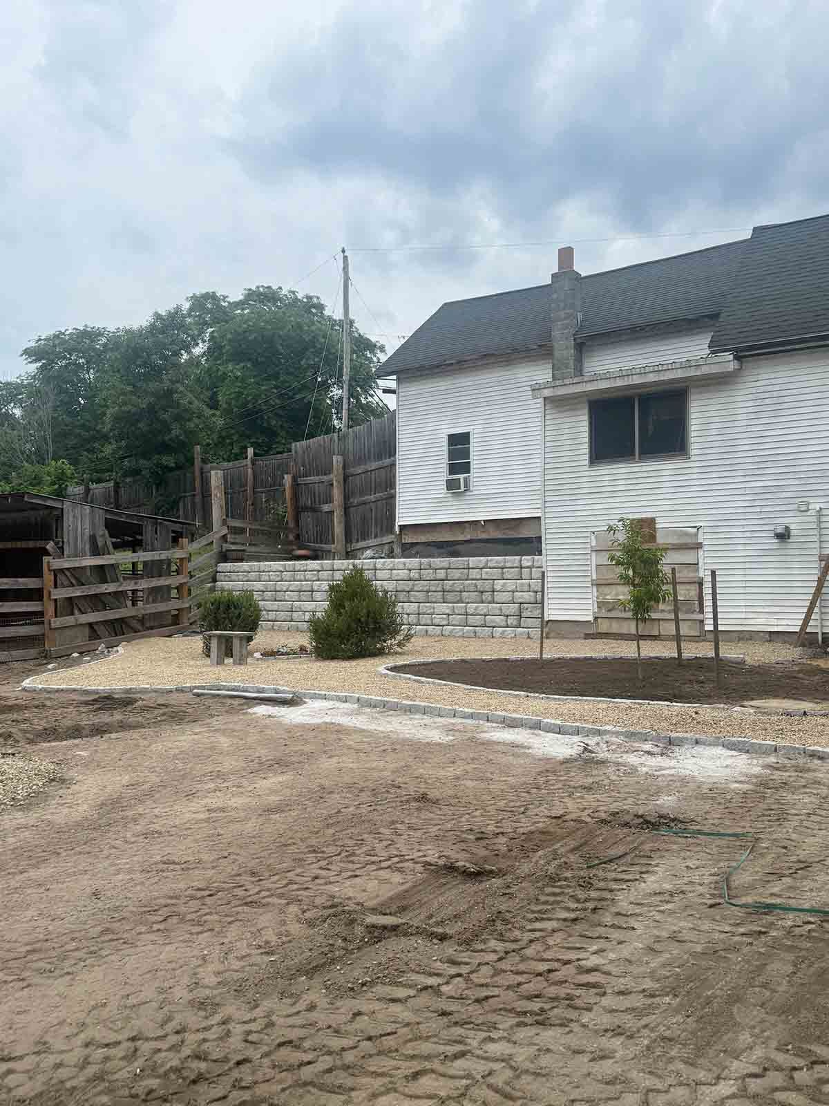 White house with a tiled roof beside a dirt yard and fence under a cloudy sky