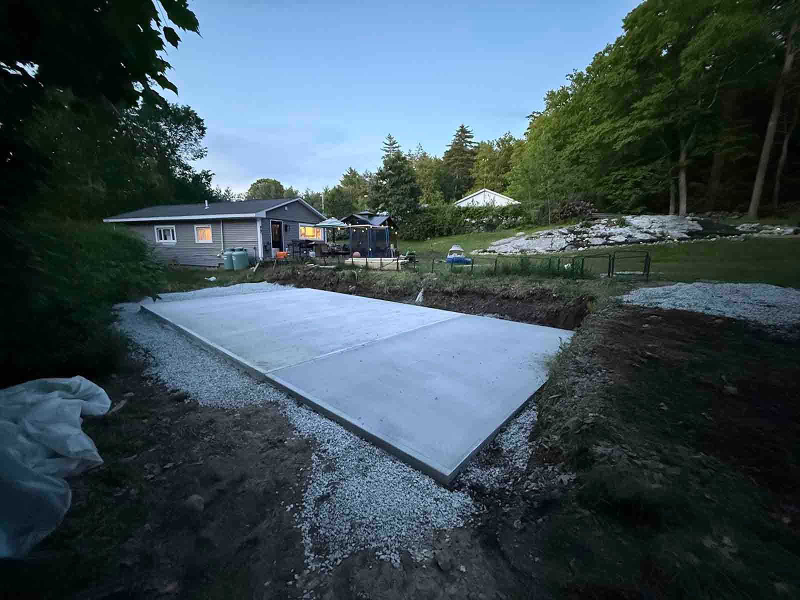 Freshly poured concrete slab beside a house, with trees and a yard in the background.