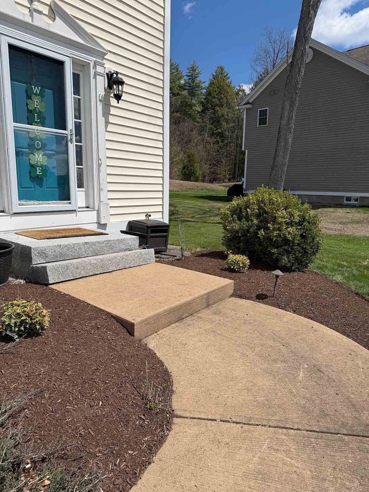 Front walkway and steps leading to a blue front door with white siding and landscaped mulch beds