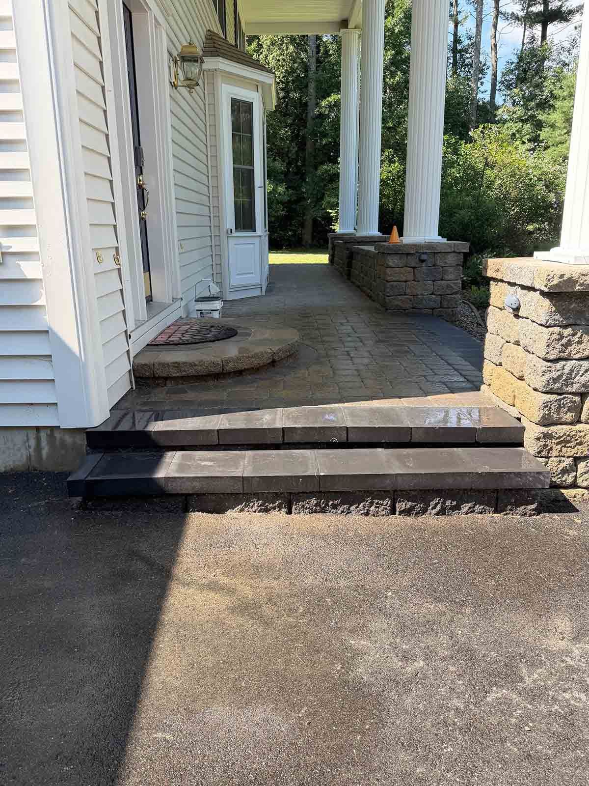 House entrance with two steps, brick walkway, and white columns beside a driveway