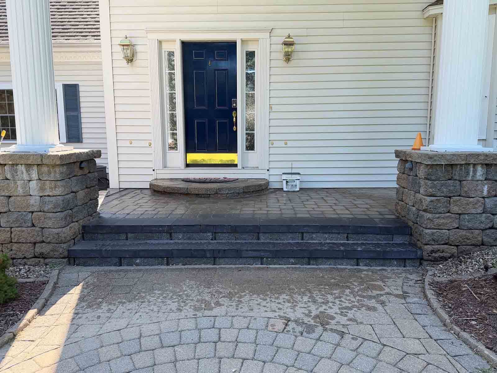 Front porch with stone steps, dark front door, and white siding, viewed from a paved driveway.