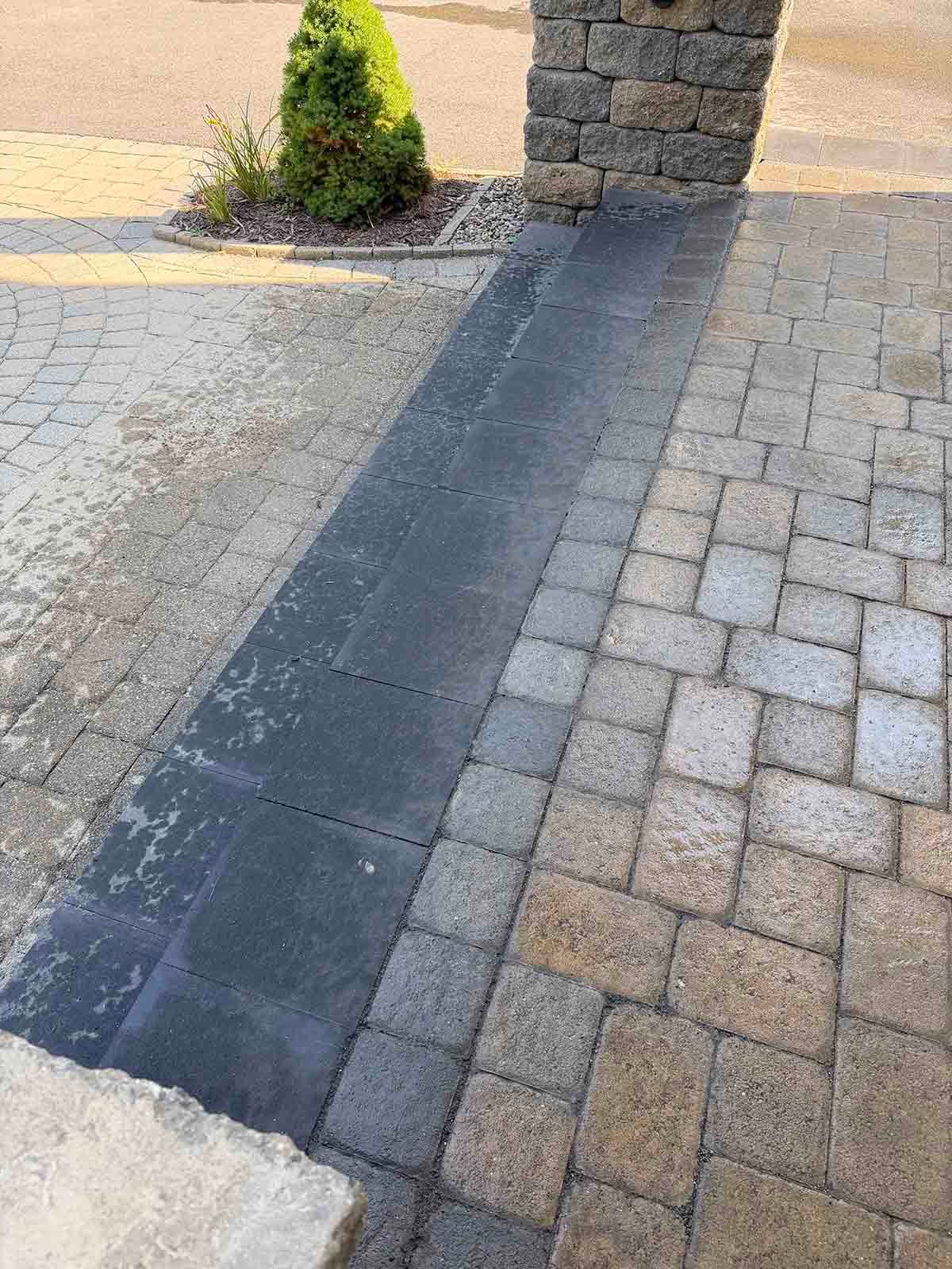 Stone paving with a dark strip running between two paved surfaces beside a stone pillar and small shrub