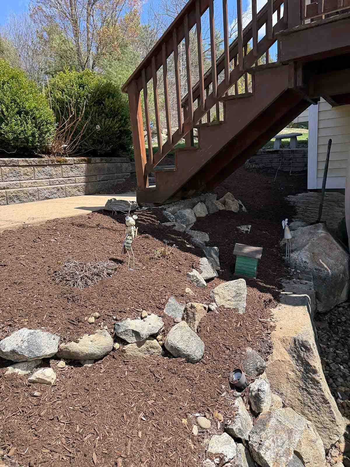 Wooden deck stairs over a landscaped rock bed with mulch and stone retaining wall