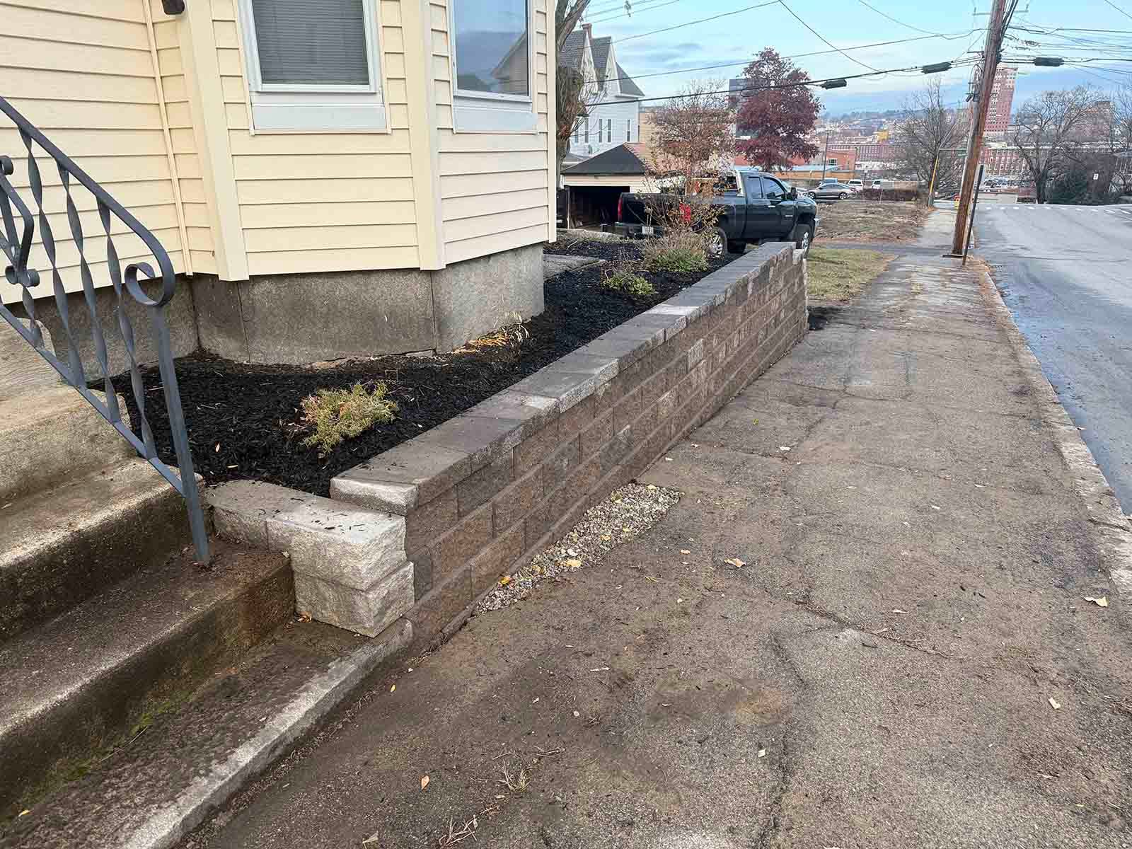 Residential house entrance with stone retaining wall and narrow sidewalk along a street