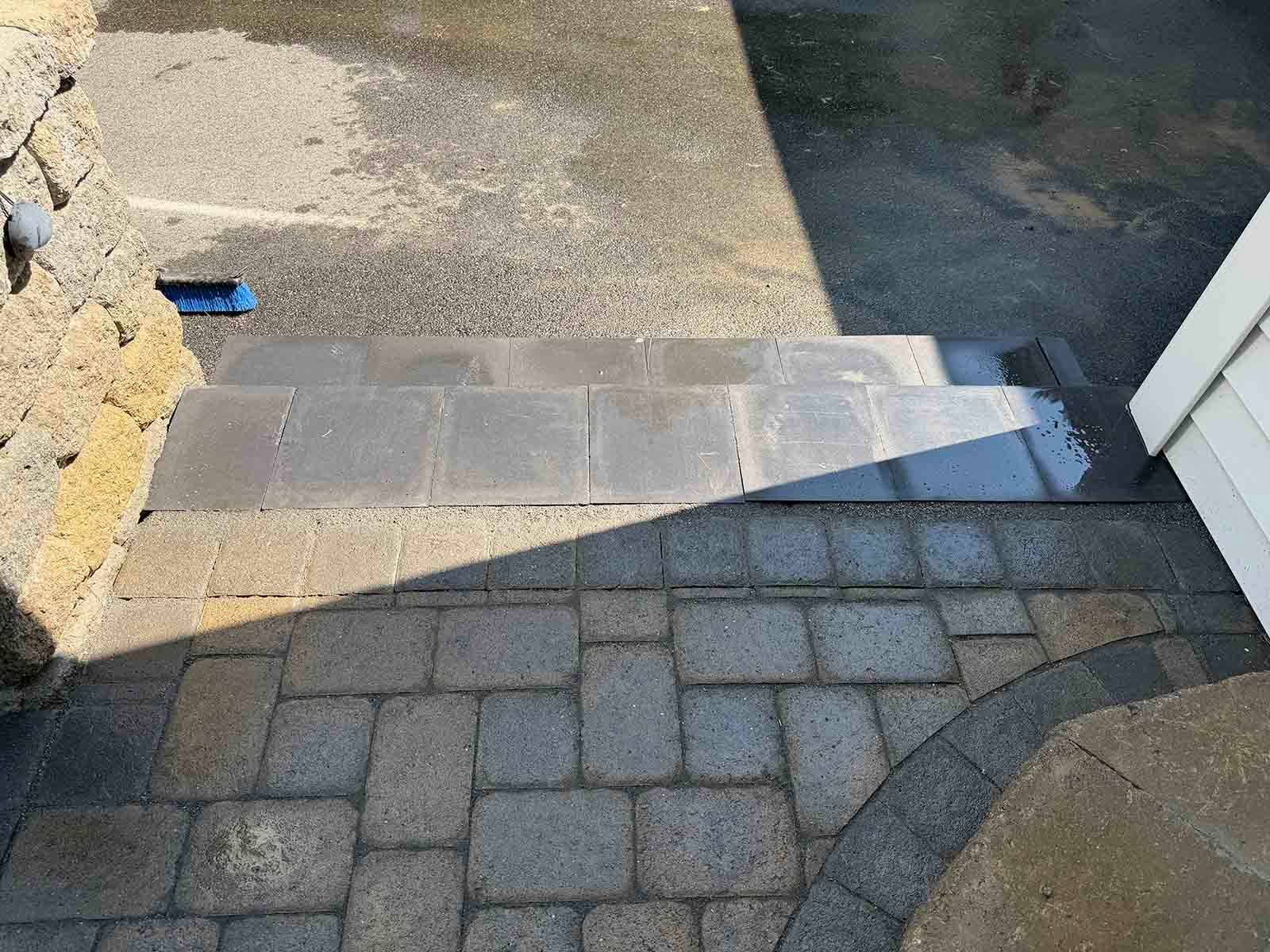 Outdoor stone path with a short ramp leading to a doorway and a narrow water channel on the right.