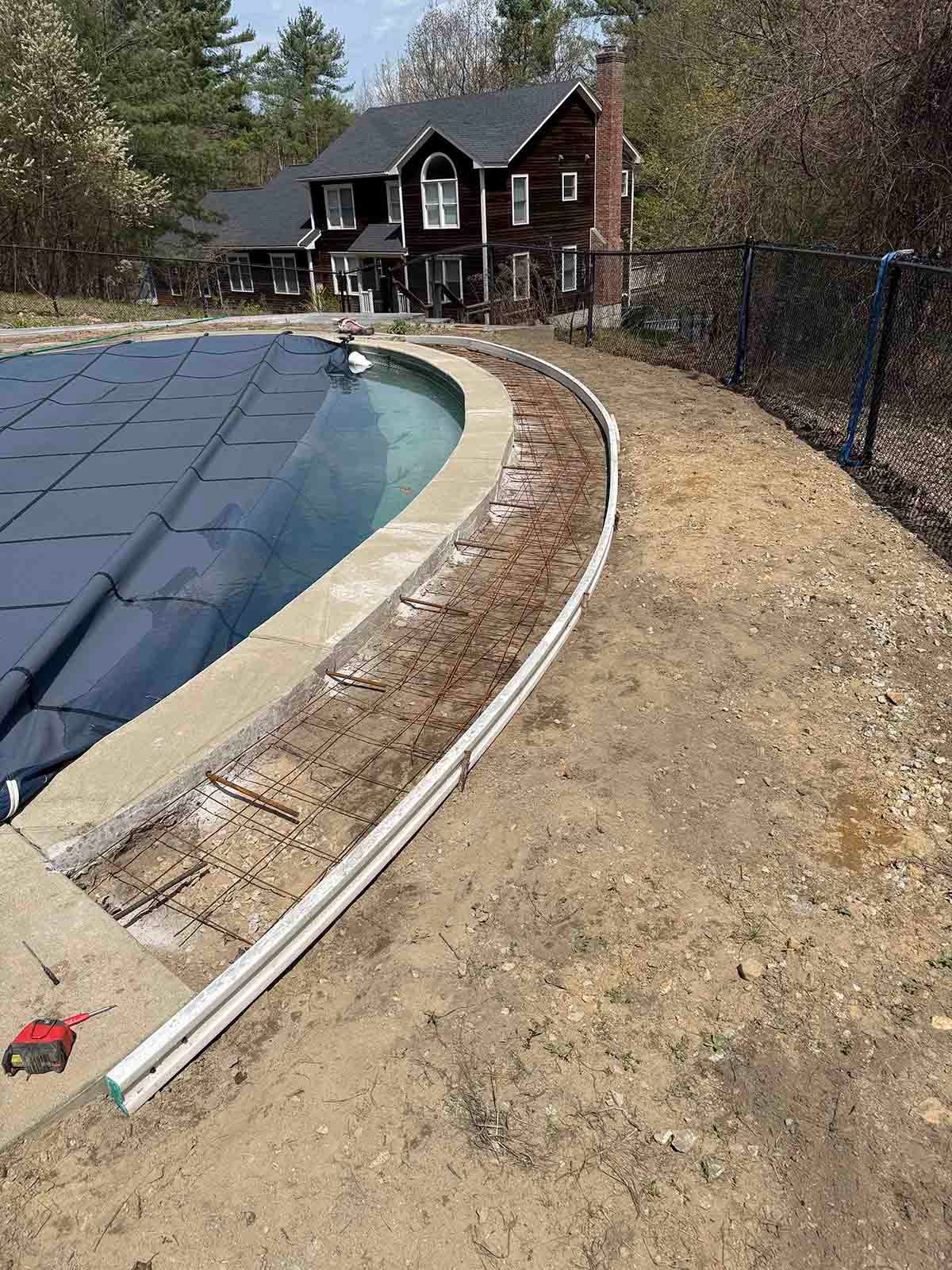 Backyard pool with blue cover, curved concrete edge, and two-story house in the background