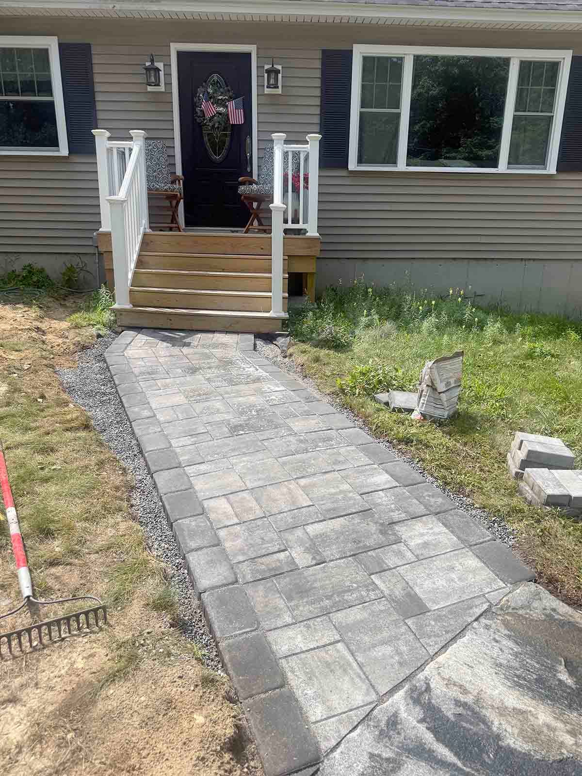 Stone walkway leads to front porch of a house under construction, with steps and siding visible.